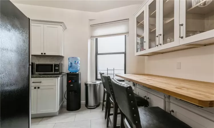 Kitchen featuring wooden counters, light tile patterned floors, white cabinets, and tasteful backsplash