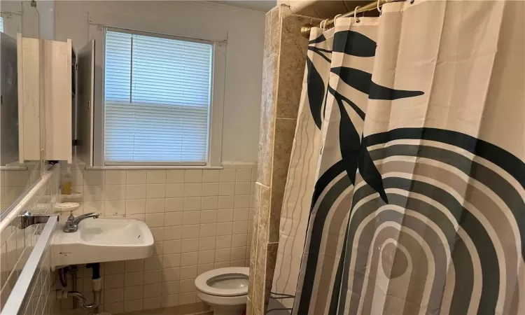 Bathroom with backsplash, crown molding, tile walls, toilet, and sink