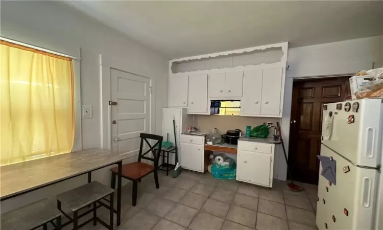 Kitchen with white cabinetry, light tile patterned flooring, and white fridge