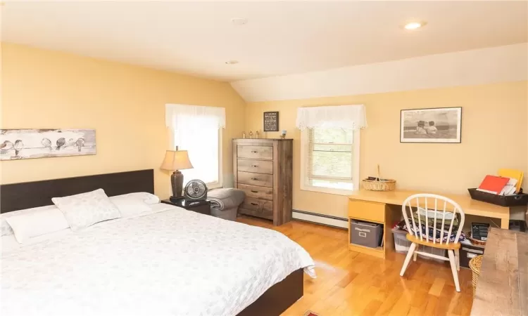 Bedroom featuring baseboard heating, vaulted ceiling, multiple windows, and light hardwood / wood-style floors