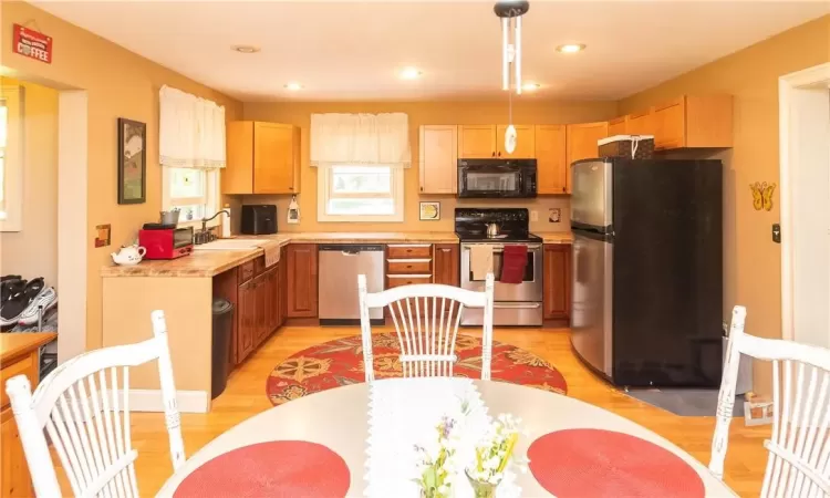 Kitchen with pendant lighting, stainless steel appliances, sink, light brown cabinets, and light hardwood / wood-style floors