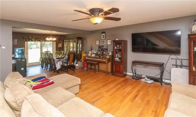 Living room with ceiling fan with notable chandelier, a baseboard radiator, and light hardwood / wood-style flooring