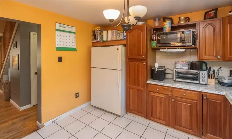 Kitchen featuring light wood-type flooring, a chandelier, backsplash, light stone counters, and white refrigerator