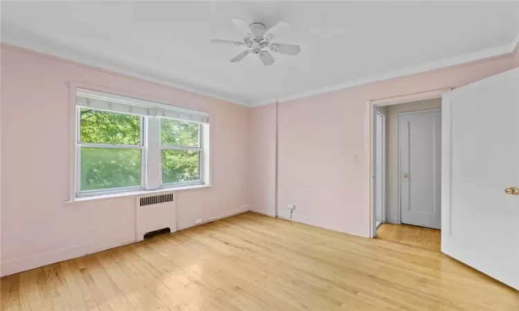 Unfurnished room featuring radiator heating unit, light wood-type flooring, crown molding, and ceiling fan