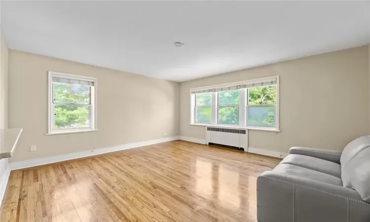 Unfurnished living room featuring radiator, plenty of natural light, and light hardwood / wood-style floors