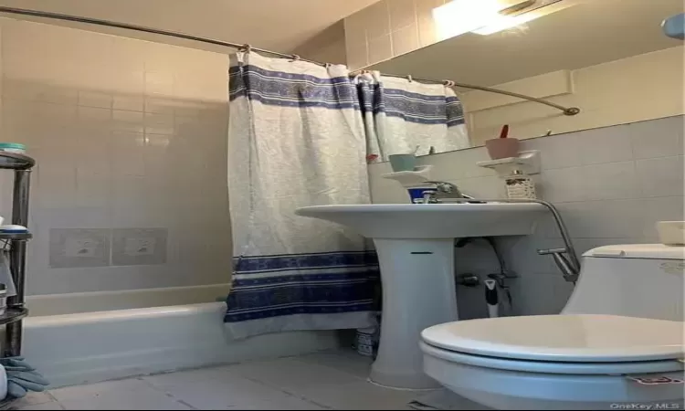 Bathroom featuring shower / bath combination with curtain, toilet, and tile walls