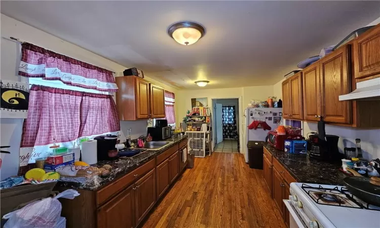 Kitchen with a wealth of natural light, dark wood-type flooring, ventilation hood, sink, and white appliances