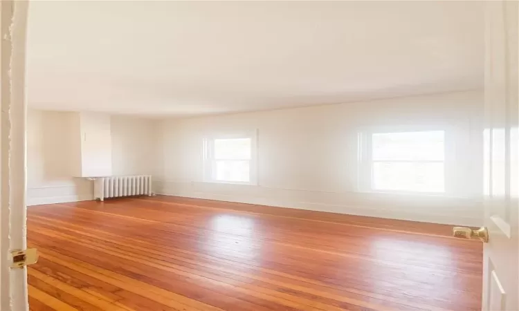 Empty room with light hardwood / wood-style flooring and radiator heating unit