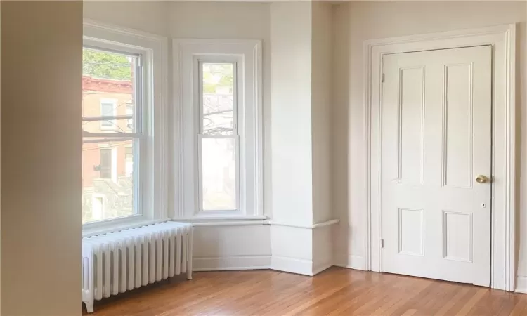 Empty room with light hardwood / wood-style floors and radiator heating unit