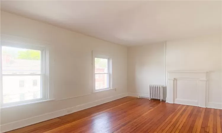 Empty room with radiator, hardwood / wood-style floors, and plenty of natural light