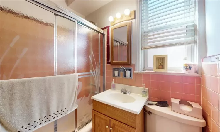 Bathroom unit 2 featuring decorative backsplash, vanity, tile walls, an enclosed shower, and toilet