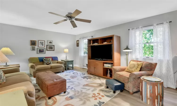 Living room with ceiling fan, a healthy amount of sunlight, a baseboard heating unit, and light hardwood / wood-style flooring