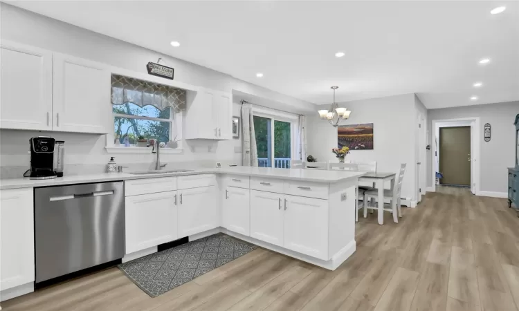 Kitchen featuring stainless steel dishwasher, white cabinets, light wood-type flooring, and sink