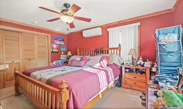 Carpeted bedroom with ceiling fan, a closet, and a wall mounted air conditioner