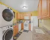 Kitchen featuring light brown cabinetry, sink, white appliances, and stacked washing maching and dryer