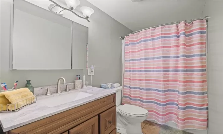 Bathroom with curtained shower, tile patterned floors, vanity, and toilet