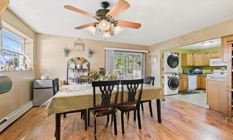 Dining area featuring stacked washer and clothes dryer, baseboard heating, light wood-type flooring, and a wealth of natural light