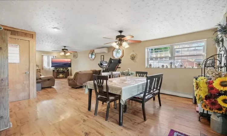 Dining space featuring light hardwood / wood-style floors, ceiling fan, baseboard heating, a wall mounted AC, and a textured ceiling