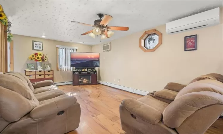 Living room featuring ceiling fan, hardwood / wood-style flooring, a baseboard heating unit, and an AC wall unit