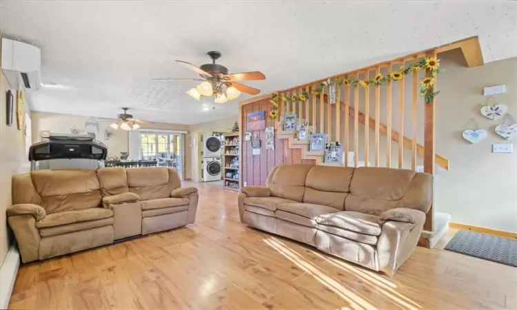 Living room featuring ceiling fan, a textured ceiling, hardwood / wood-style floors, and stacked washing maching and dryer