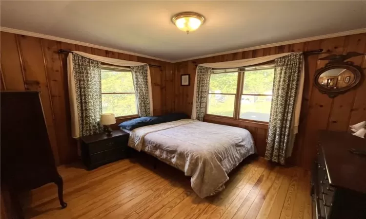 Bedroom with ornamental molding, multiple windows, wooden walls, and light hardwood / wood-style floors