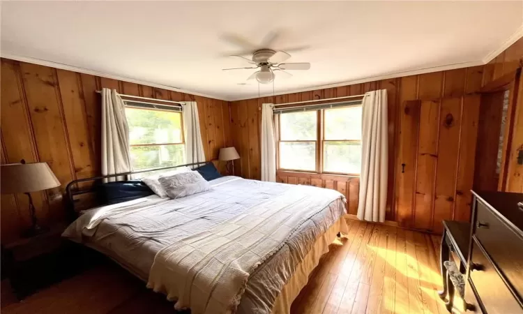 Bedroom with wooden walls, hardwood / wood-style flooring, multiple windows, and ceiling fan