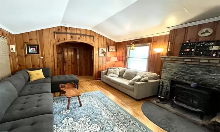 Living room with a wood stove, light hardwood / wood-style floors, crown molding, vaulted ceiling, and wood walls