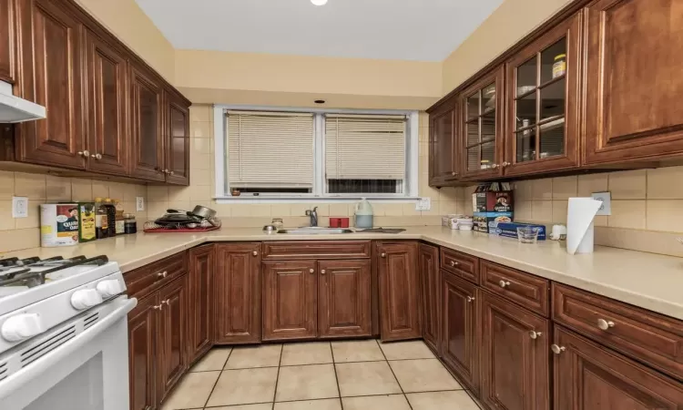 Kitchen featuring light tile patterned flooring, white gas range oven, sink, and backsplash