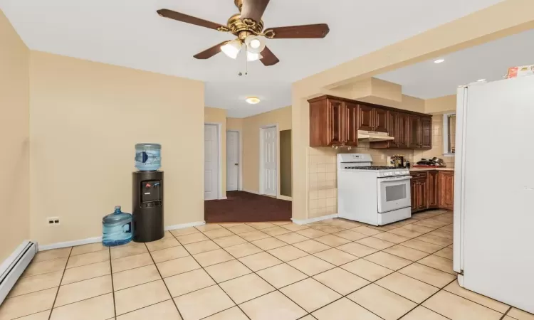 Kitchen featuring white appliances, a baseboard heating unit, light tile patterned floors, and ceiling fan