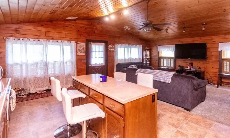 Kitchen featuring wood walls, ceiling fan, a kitchen island, wood ceiling, and lofted ceiling