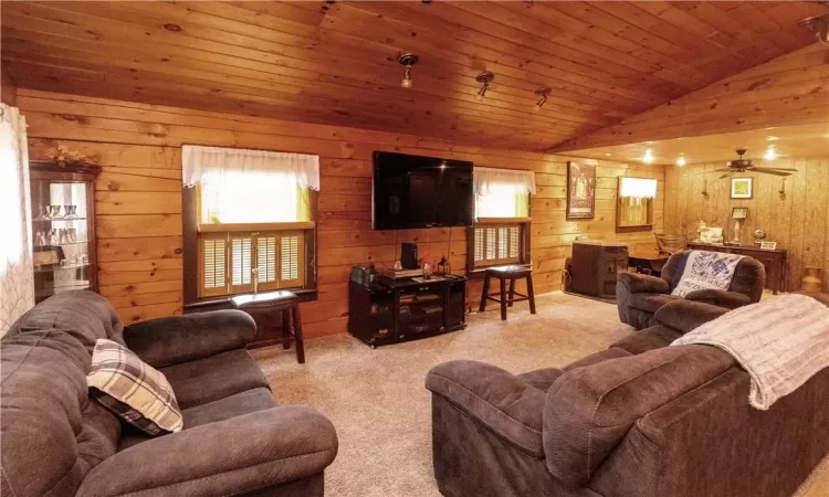 Carpeted living room with ceiling fan, wood walls, vaulted ceiling, and wood ceiling