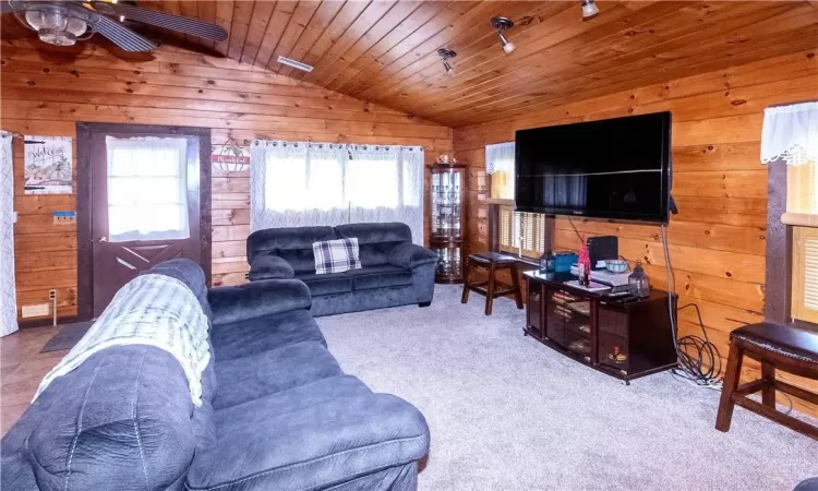 Carpeted living room featuring ceiling fan, wooden walls, wood ceiling, and vaulted ceiling