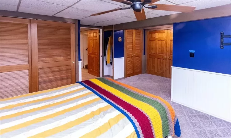 Lower level bedroom with carpet floors, wood walls, a drop ceiling, and ceiling fan