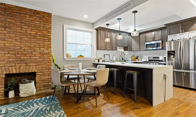 Kitchen featuring light wood-type flooring, appliances with stainless steel finishes, decorative light fixtures, and a kitchen breakfast bar