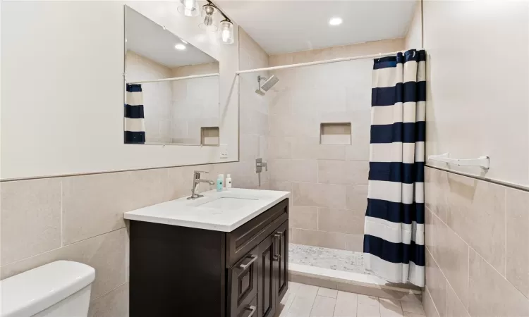 Bathroom with a shower with curtain, vanity, toilet, and tile walls