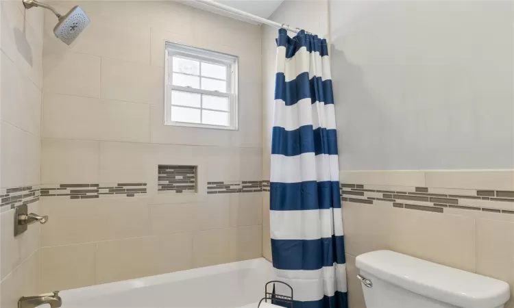 Bathroom featuring shower / bath combination with curtain, toilet, and tile walls