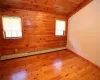 Guest bedroom with a baseboard radiator, wood ceiling, wood walls, and light hardwood / wood-style flooring