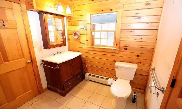 Bathroom featuring vanity, wood walls, a baseboard heating unit, tile patterned floors, and toilet