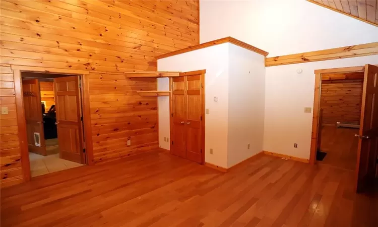 Unfurnished bedroom with wood walls, light wood-type flooring, a closet, high vaulted ceiling, and a baseboard heating unit