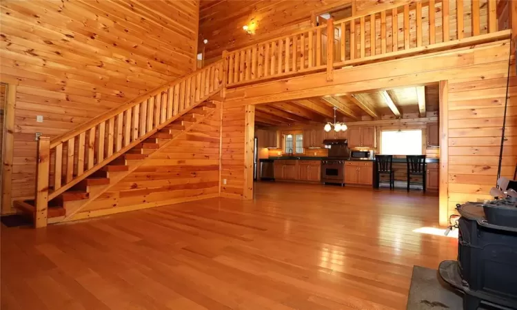 Unfurnished living room with beamed ceiling, sink, wooden walls, a chandelier, and light wood-type flooring