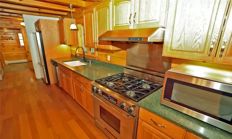 Kitchen with light hardwood / wood-style floors, stainless steel appliances, wood walls, and sink