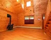 Unfurnished living room featuring high vaulted ceiling, wooden walls, and a wood stove