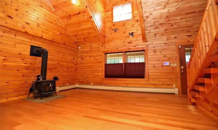 Unfurnished living room featuring high vaulted ceiling, wooden walls, and a wood stove