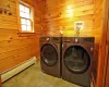 Washroom featuring washing machine and clothes dryer, wooden walls, and a baseboard radiator