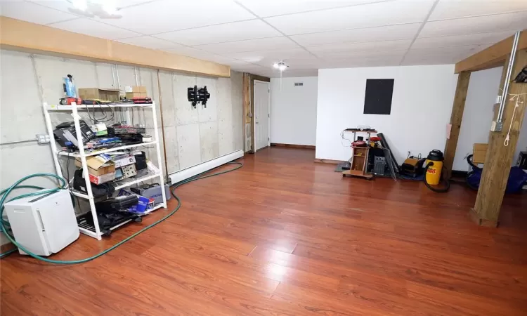 Basement featuring a paneled ceiling, wood-type flooring, electric panel, and a baseboard heating unit