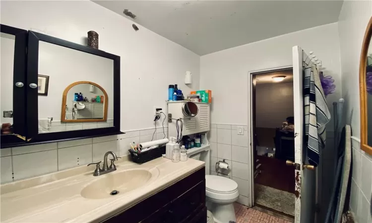 Bathroom featuring toilet, vanity, and tile walls