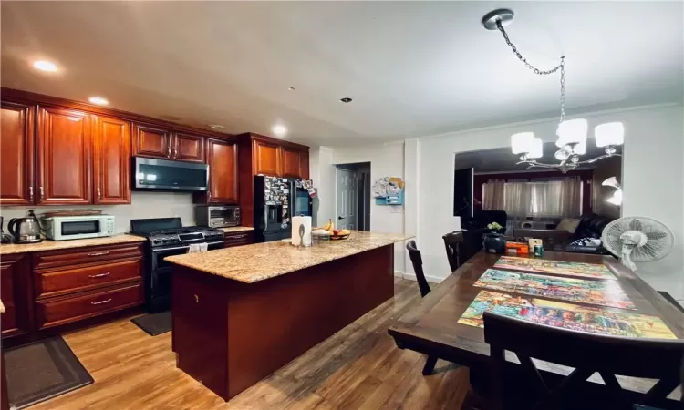 Kitchen with hardwood / wood-style flooring, black fridge, pendant lighting, a chandelier, and range with gas cooktop