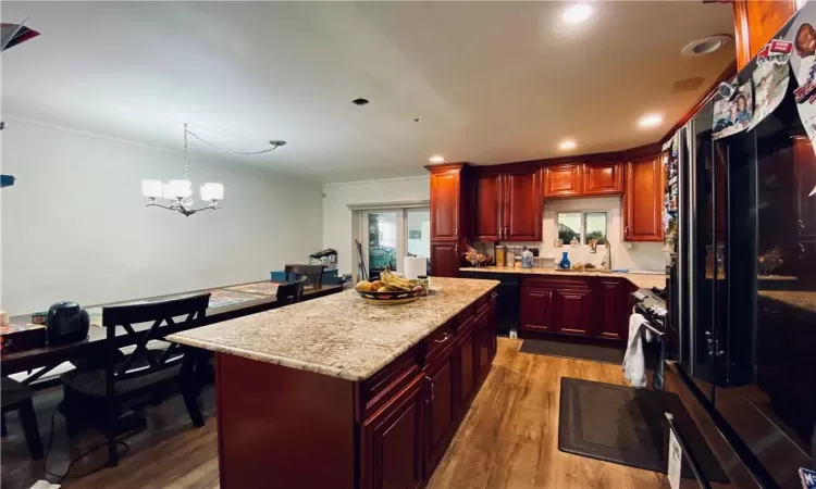 Kitchen featuring a center island, hanging light fixtures, hardwood / wood-style floors, ornamental molding, and a chandelier