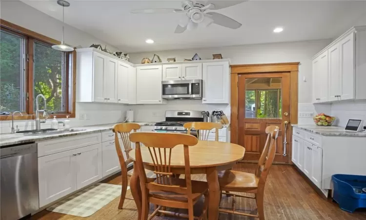 Kitchen with appliances with stainless steel finishes, light stone counters, a wealth of natural light, and white cabinetry