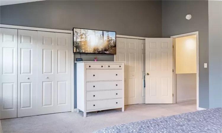 Unfurnished bedroom with multiple closets, light carpet, and high vaulted ceiling